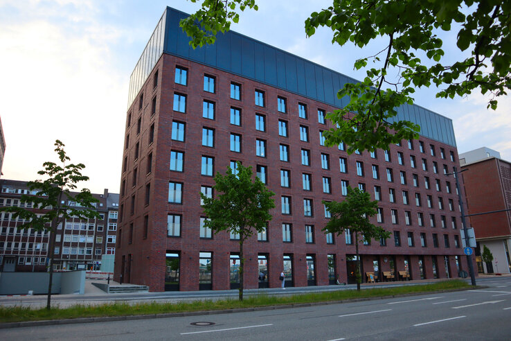 exterior view of unique by ATLANTIC Hotels Kiel Modern brick hotel with many windows, surrounded by trees, situated on a quiet street.