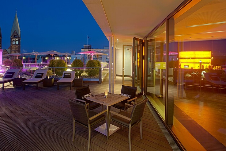 Dachterrasse des ATLANTIC Grand Hotel Bremen bei Nacht, mit Sitzbereich, Liegestühlen und beleuchteter Bar.