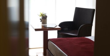 Gemütliches Hotelzimmer mit Sessel, Tisch, Pflanze und roter Bettdecke, im ATLANTIC Grand Hotel Travemünde.