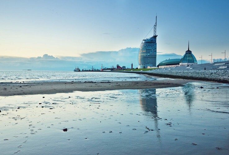 ATLANTIC Hotel Sail City in Bremerhaven, moderne Architektur am Ufer, reflektiert im ruhigen Wasser bei Sonnenuntergang.
