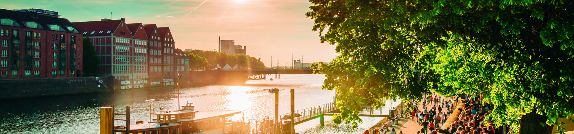 Sunset on the Weser promenade in Bremen with people, boats and historic buildings in the background.