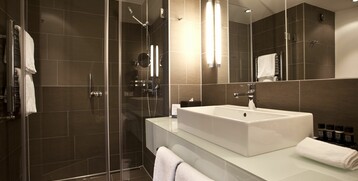 Modern bathroom with walk-in shower, large washbasin and stylish lighting at the ATLANTIC Grand Hotel Bremen.