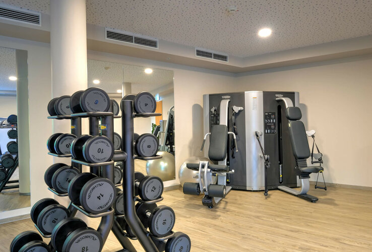 Fitness room at the ATLANTIC Hotel Airport Bremen with weights and fitness equipment on a light wooden floor.