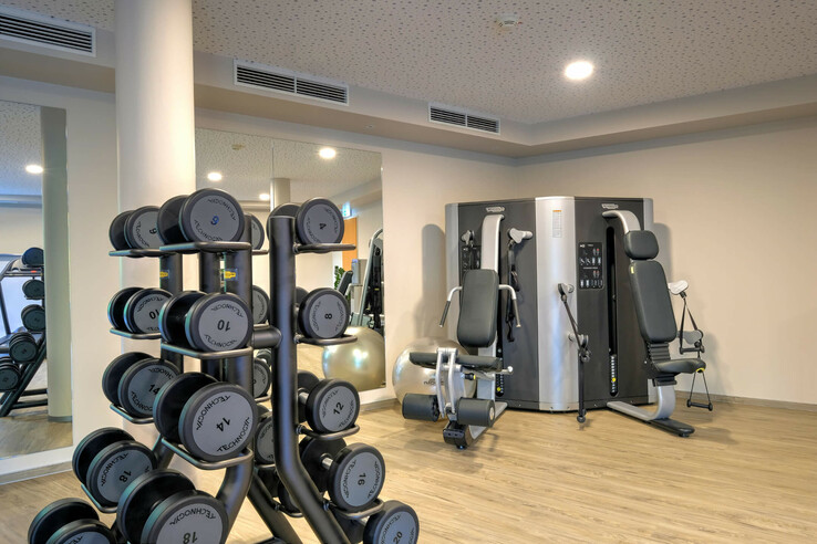 Fitness room at the ATLANTIC Hotel Airport Bremen with weights and fitness equipment on a light wooden floor.