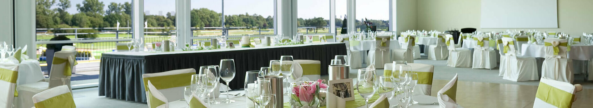 Elegant banquet hall in the ATLANTIC Hotel Galopprennbahn, Bremen, with set tables and a view of the racecourse.