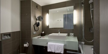 Modernes Badezimmer im ATLANTIC Grand Hotel Bremen mit Waschbecken, Spiegel, Dusche und WC in elegantem Design.