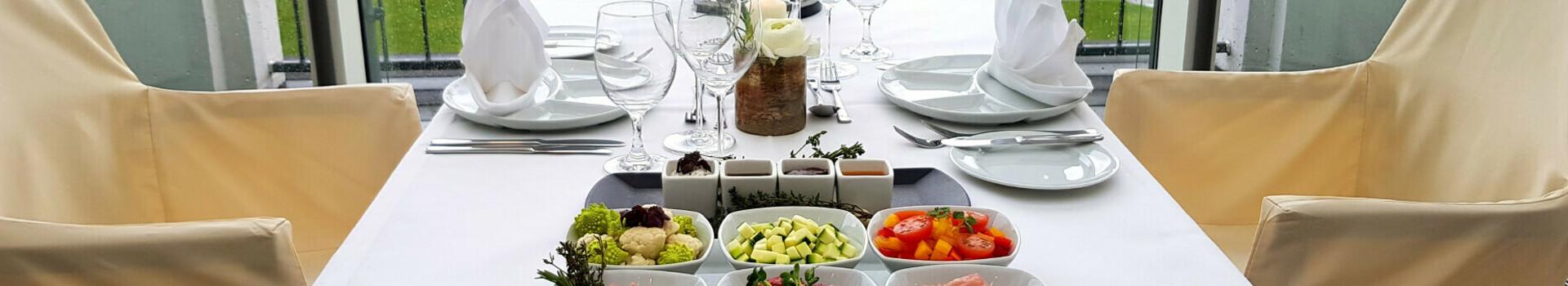 Eleganter, gedeckter Tisch mit Gourmet-Vorspeisen und Blick auf den Garten im ATLANTIC Grand Hotel Travemünde.
