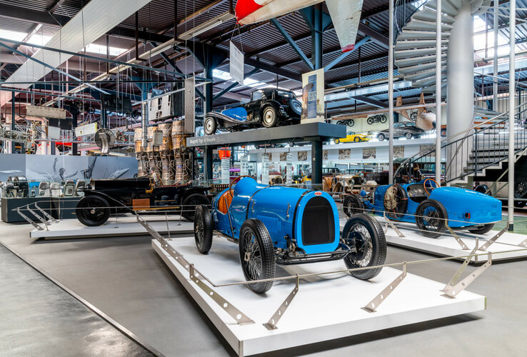 Vintage car exhibition in the museum with blue racing cars and historic vehicles, surrounded by industrial architecture.