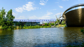 ATLANTIC Hotel Universum in Bremen neben einem See, moderner Bau, blauer Himmel, grüne Ufervegetation.