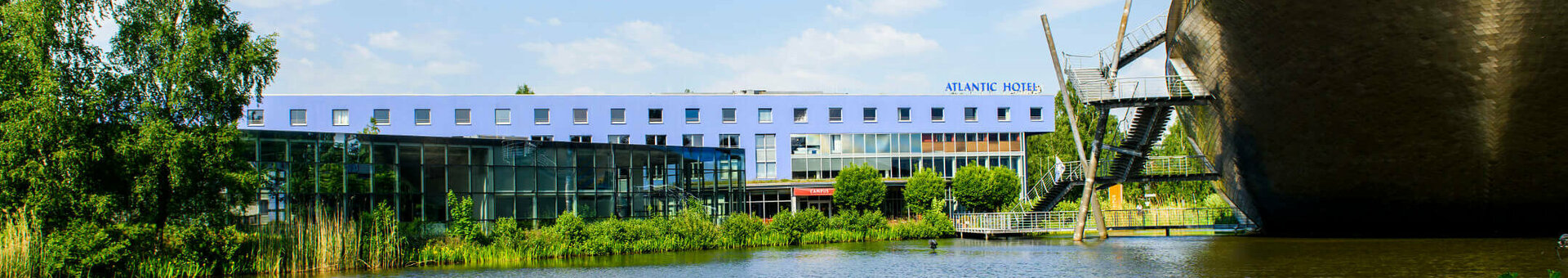 ATLANTIC Hotel Universum in Bremen next to a lake, modern building, blue sky, green shore vegetation.