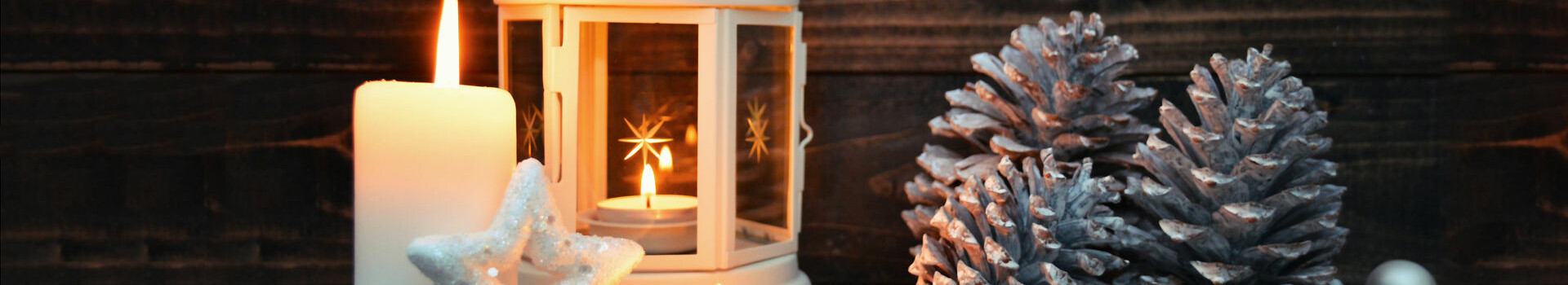 Candles, lantern and silver pine cones on a snow-covered wooden background, decorated for Christmas.