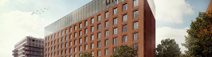 Backstein-Hotelgebäude mit großen Fenstern, Bäumen davor und Menschen auf dem Gehweg bei Tageslicht.