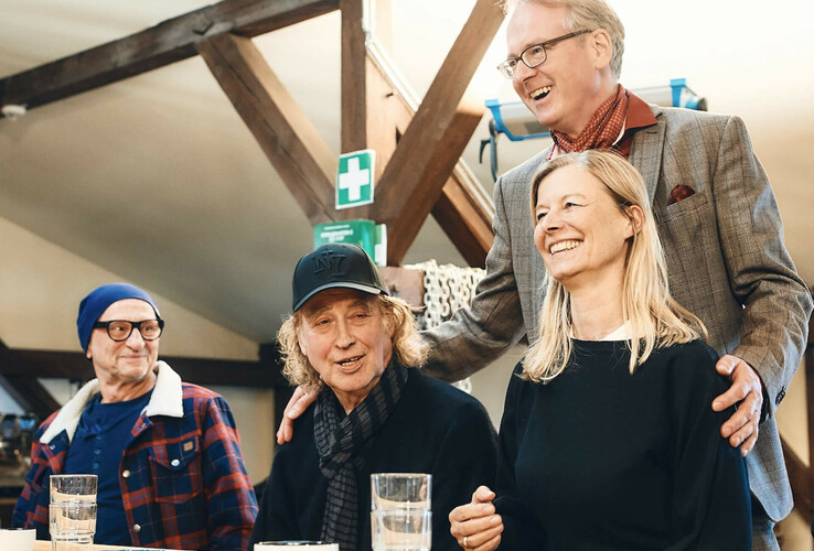 Vier lachende Personen sitzen an einem Tisch in einem gemütlichen Raum.