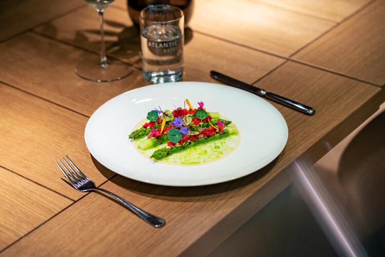 Ein kunstvoll angerichteter Salat mit Spargel und Blüten auf einem weißen Teller im ATLANTIC Hotel Münster.