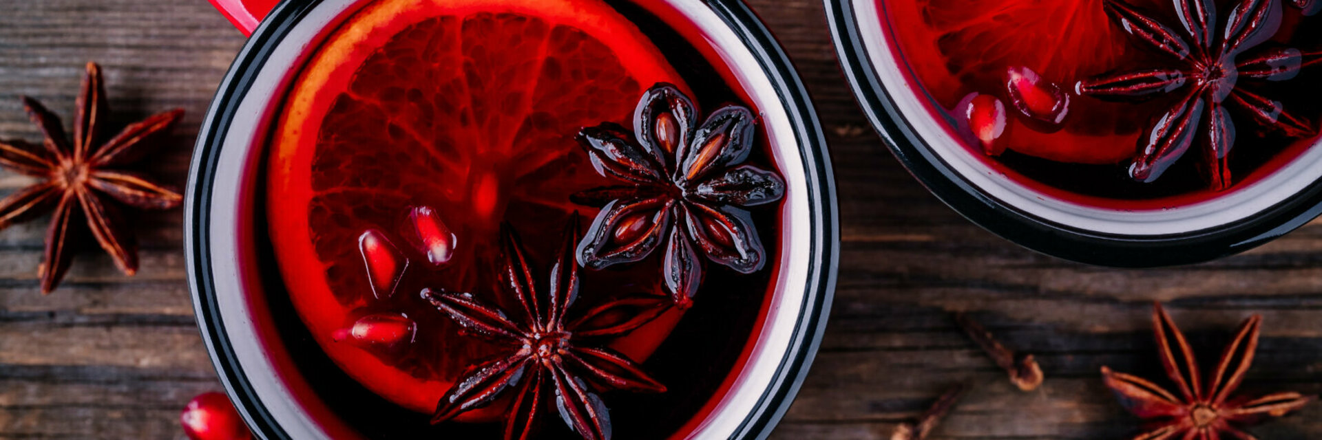Zwei Becher mit rotem Glühwein und einer Orangenscheibe