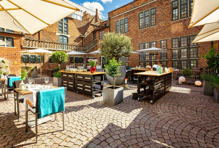 Paved inner courtyard of the ATLANTIC Grand Hotel Bremen with tables, parasols and plants.