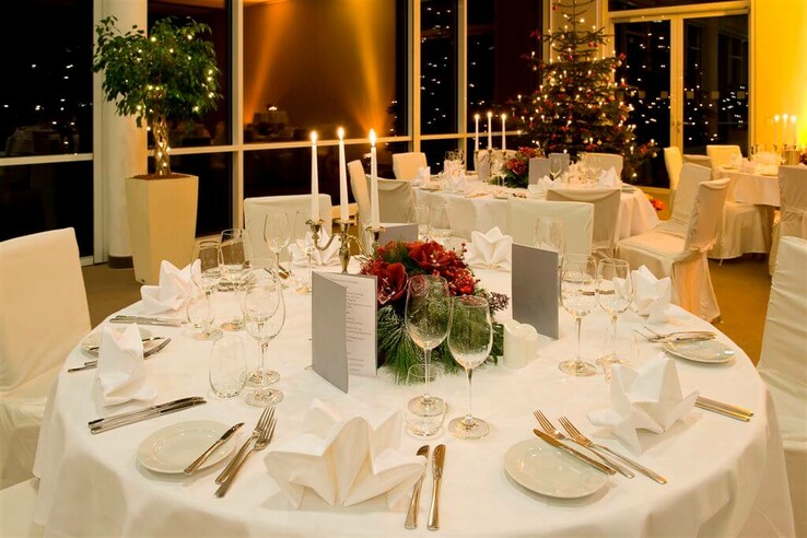 Festlich gedeckter Tisch in elegantem Restaurant mit Kerzenlicht und Weihnachtsbaum im ATLANTIC Hotel Galopprennbahn.