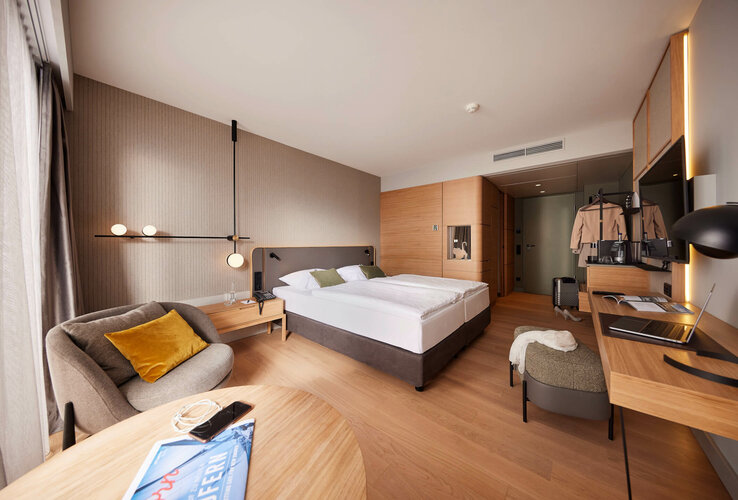 Modernes Hotelzimmer mit Doppelbett, Schreibtisch, Sessel, Garderobe und warmem Holzdekor im ATLANTIC Hotel Heidelberg.