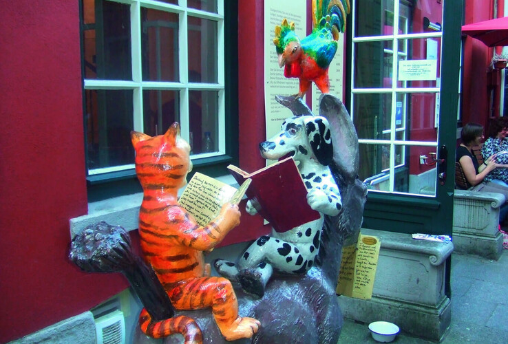 Skulptur der Bremer Stadtmusikanten: Katze, Hund und Hahn lesen Bücher vor roter Wand, neben einem Fenster.