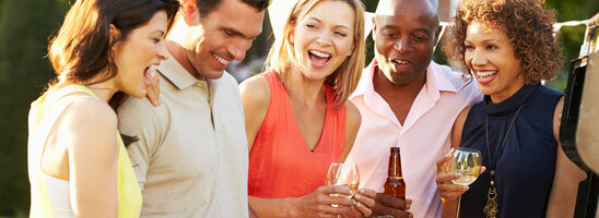 Gruppe fröhlicher Menschen bei Grillparty im Freien, mit Getränken und Essen, unter Wimpelgirlande.