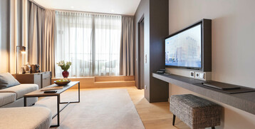 Modern hotel room with sofa, coffee table, TV, large windows and bright furnishings at the ATLANTIC Grand Hotel Bremen.