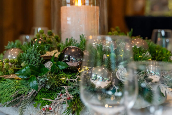 Festlich gedeckter Tisch mit Kerze in einem Kranz aus Tannenzweigen und silbernen Kugeln im ATLANTIC Hotel Landgut Horn Bremen.