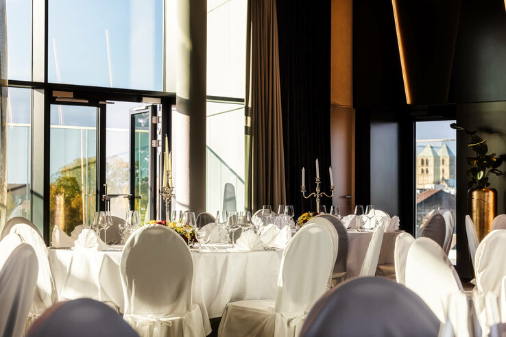 Eleganter, lichtdurchfluteter Bankettsaal mit gedeckten Tischen und Blick auf die Stadt im ATLANTIC Hotel Münster.