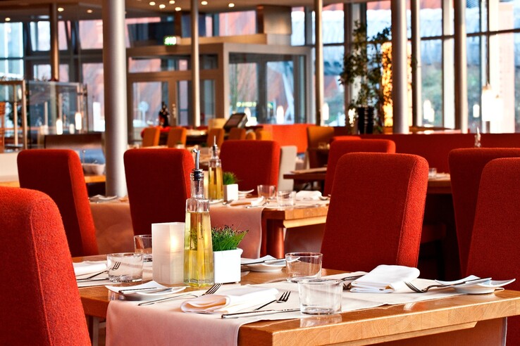 Elegantes Hotelrestaurant mit rot gepolsterten Stühlen, gedeckten Holztischen und großen Fenstern im ATLANTIC Hotel Universum.