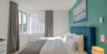 Bright hotel room with double bed, turquoise wall, large window and modern furnishings at the ATLANTIC Grand Hotel Travemünde.