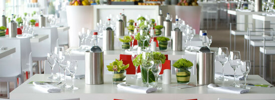 Elegantes Restaurant im ATLANTIC Hotel Bremen mit gedeckten Tischen, Blumen und einem Koch im Hintergrund.