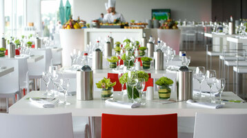 Elegantes Restaurant im ATLANTIC Hotel Bremen mit gedeckten Tischen, Blumen und einem Koch im Hintergrund.