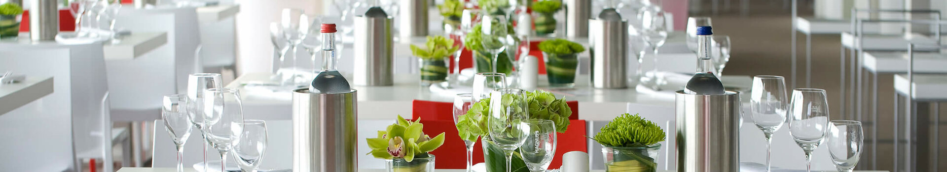 Elegantes Restaurant im ATLANTIC Hotel Bremen mit gedeckten Tischen, Blumen und einem Koch im Hintergrund.
