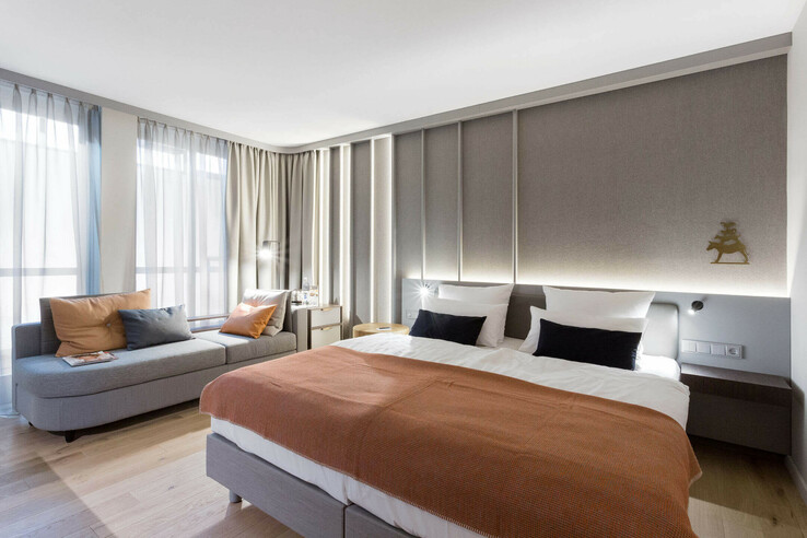Modern hotel room with double bed, cozy seating area, light curtains and stylish wall decorations.