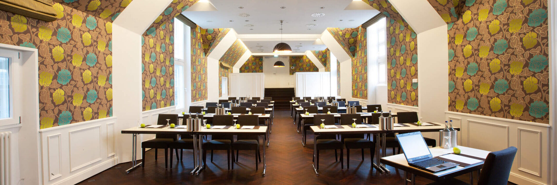 Moderner Konferenzraum im ATLANTIC Grand Hotel Bremen mit stilvoller Tapete und Tischen in Reihen.