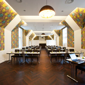 Parlimentary seating in the Scotland Saal of the ATLANTIC Grand Hotel Bremen Modern conference room in the ATLANTIC Grand Hotel Bremen with stylish wallpaper and rows of tables.