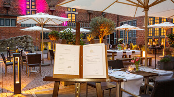 Gemütlicher Hotel-Innenhof mit gedeckten Tischen, Sonnenschirmen und stimmungsvoller Beleuchtung am Abend.