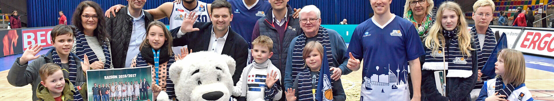 Gruppe von Menschen und Maskottchen auf einem Basketballfeld, lächelnd und posierend für ein Foto.