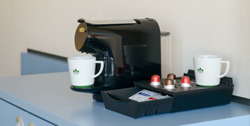 Coffee machine with cups and capsules on a blue cupboard in the ATLANTIC Hotel Sail City room.