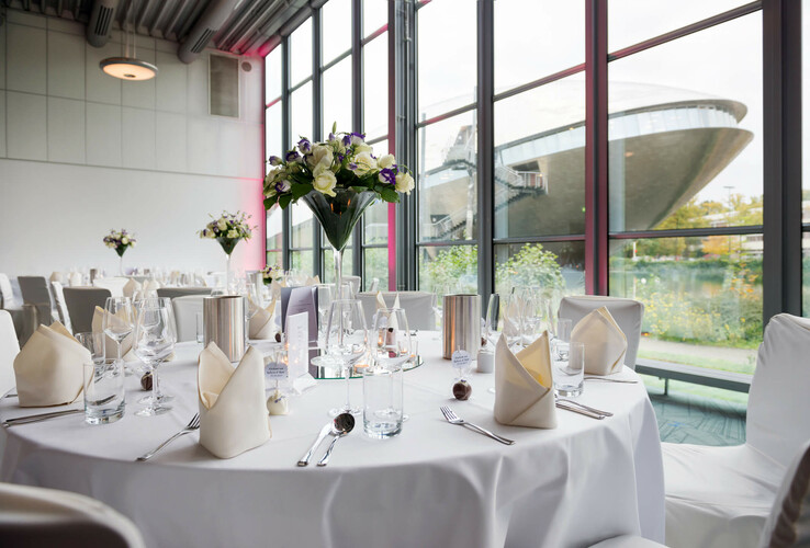 Eleganter, gedeckter Tisch in lichtdurchflutetem Raum mit Blick auf das Universum Bremen durch große Fenster.