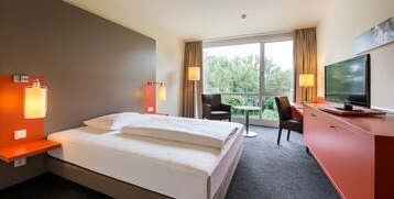Modern hotel room with large bed, desk, TV and panoramic window with a view of the countryside.