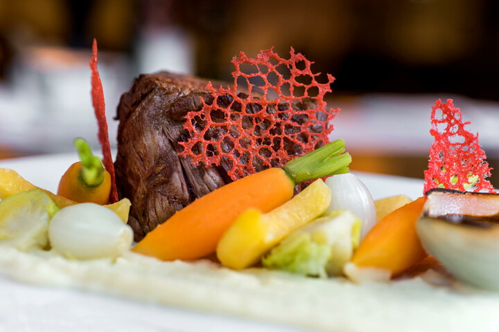 Gourmet dish with tender meat, colorful vegetables and red decoration on a white plate at the ATLANTIC Hotel Lübeck.