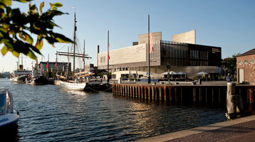 Harbor view in Bremerhaven with sailing ships and the German Emigration Center at sunset.