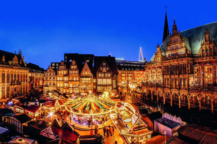 Blick auf den beleuchteten Bremer Weihnachtsmarkt bei Nacht mit historischen Gebäuden im Hintergrund.