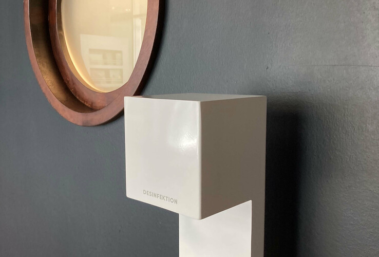 Disinfectant dispenser in front of dark gray wall with round wooden frame mirror in the ATLANTIC Hotel Sail City, Bremerhaven.