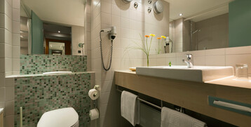 Modernes Badezimmer mit Waschbecken, Toilette, Spiegel und Dusche im ATLANTIC Hotel Universum, Bremen.