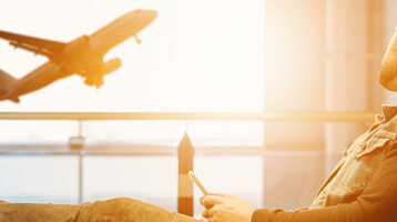 Man relaxing in the airport, looking at a plane taking off through a large window.