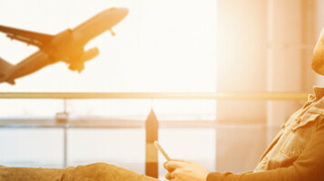 Mann entspannt im Flughafen, schaut auf startendes Flugzeug durch großes Fenster.