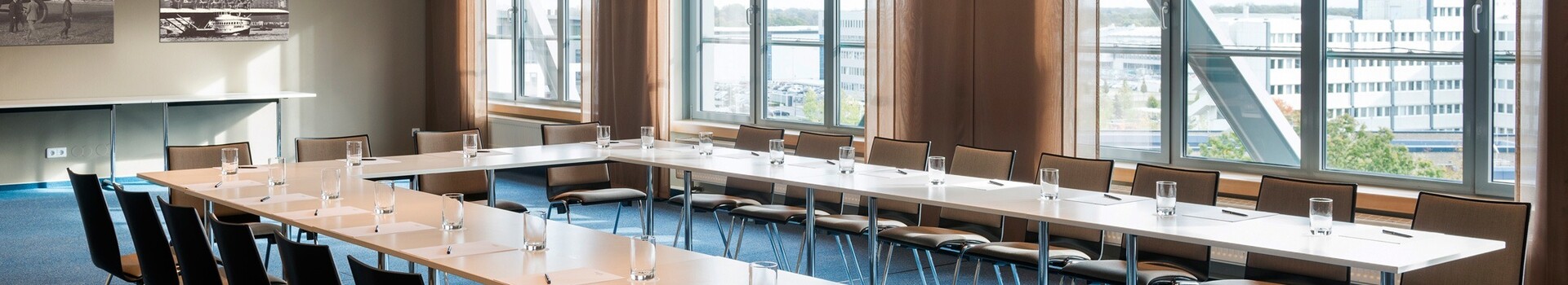ATLANTIC Hotel Airport - the Hotel with its own airport Bright conference room with U-shaped table arrangement, chairs, large windows and murals at the ATLANTIC Hotel Airport Bremen.