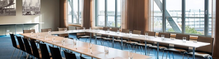 Bright conference room with U-shaped table arrangement, chairs, large windows and murals at the ATLANTIC Hotel Airport Bremen.