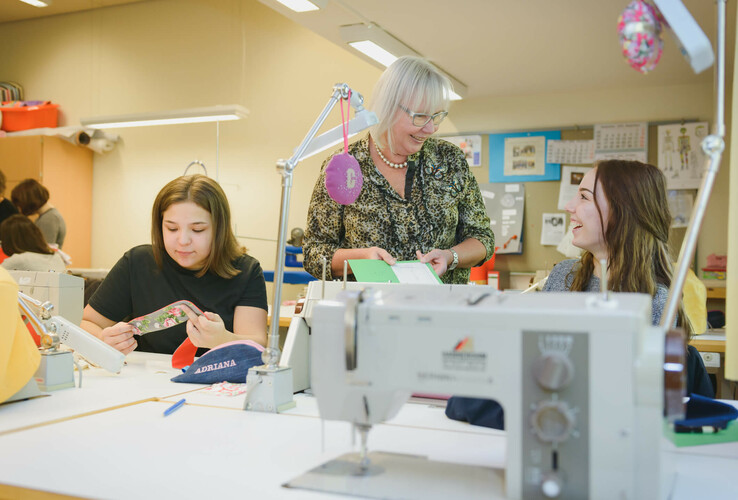 People in a sewing course, working on sewing machines and talking to each other.